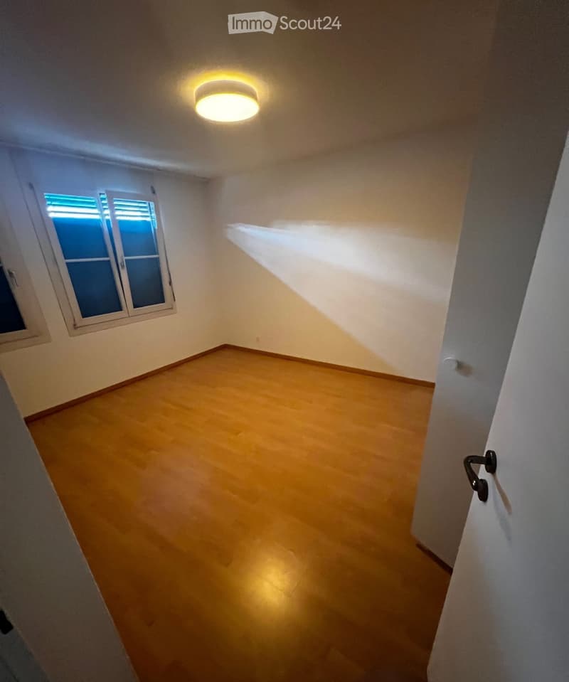 Empty room with wooden flooring, white walls, and a single window with blinds. A ceiling light fixture is visible.