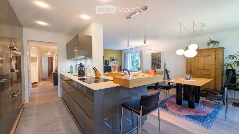 Modern kitchen with a central island, stainless steel appliances, pendant lights, and a dining area with a table and chairs.