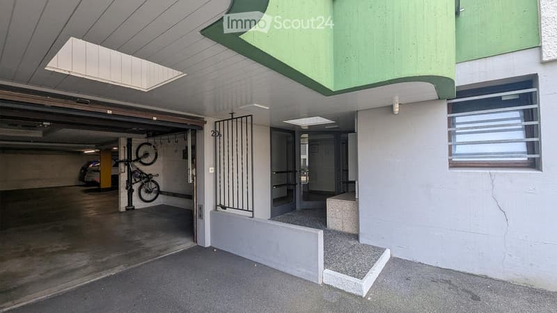 Underground parking area with concrete floors and walls, featuring a bicycle rack with two bicycles, a car parked inside, and a gated entrance leading to another section.