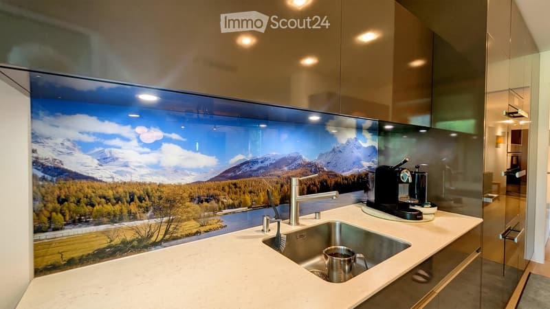 Modern kitchen with a large panoramic mural of a mountain landscape, a stainless steel sink, a coffee maker, and a cup on the counter.