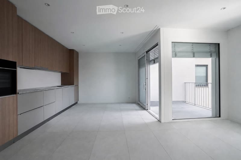 Empty kitchen with modern wooden cabinets, white countertops, and a large sliding glass door leading to a balcony.