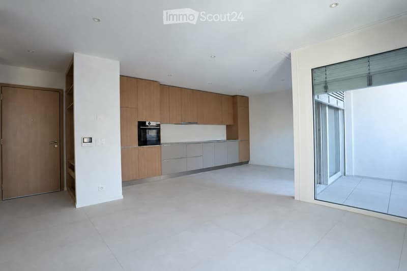 Modern kitchen with light wooden cabinets, stainless steel oven, and large glass sliding doors leading to a balcony.