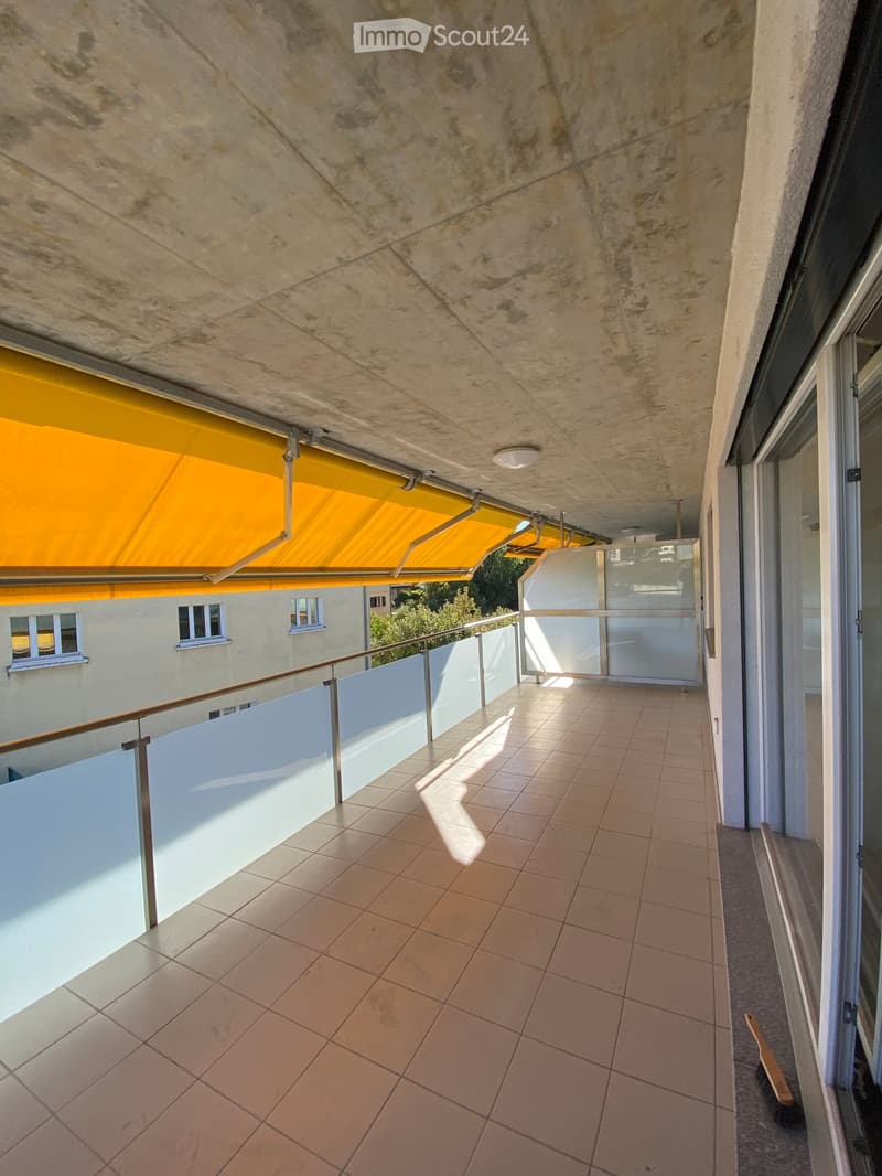 Balcony with tiled floor, glass railing, and yellow awning overhead.