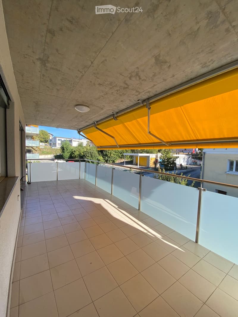 Balcony with tiled floor, glass railing, and yellow retractable awning.