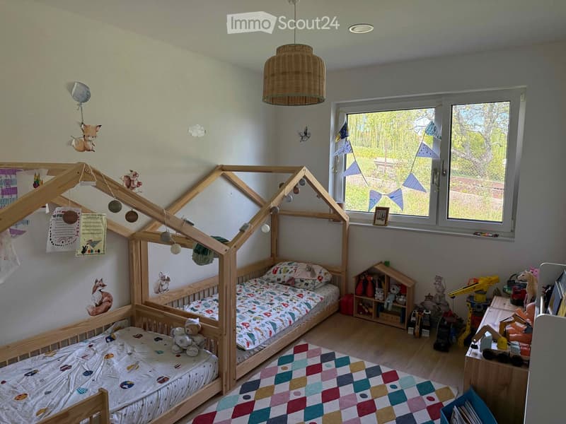 A well-lit children's bedroom with a wooden loft bed, colorful bedding, toys, and a hanging basket lamp.