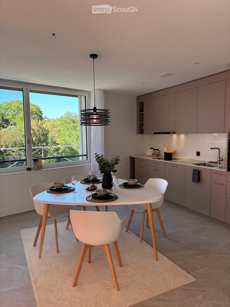 Modern kitchen and dining area with a white dining table, four white chairs, grey cabinets, a sink, and a pendant light fixture.