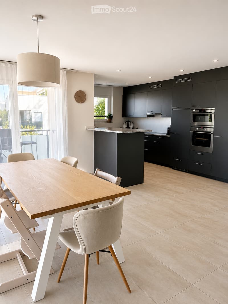 Modern kitchen with dark cabinets, a central island, a dining table with chairs, and built-in appliances including an oven and microwave.