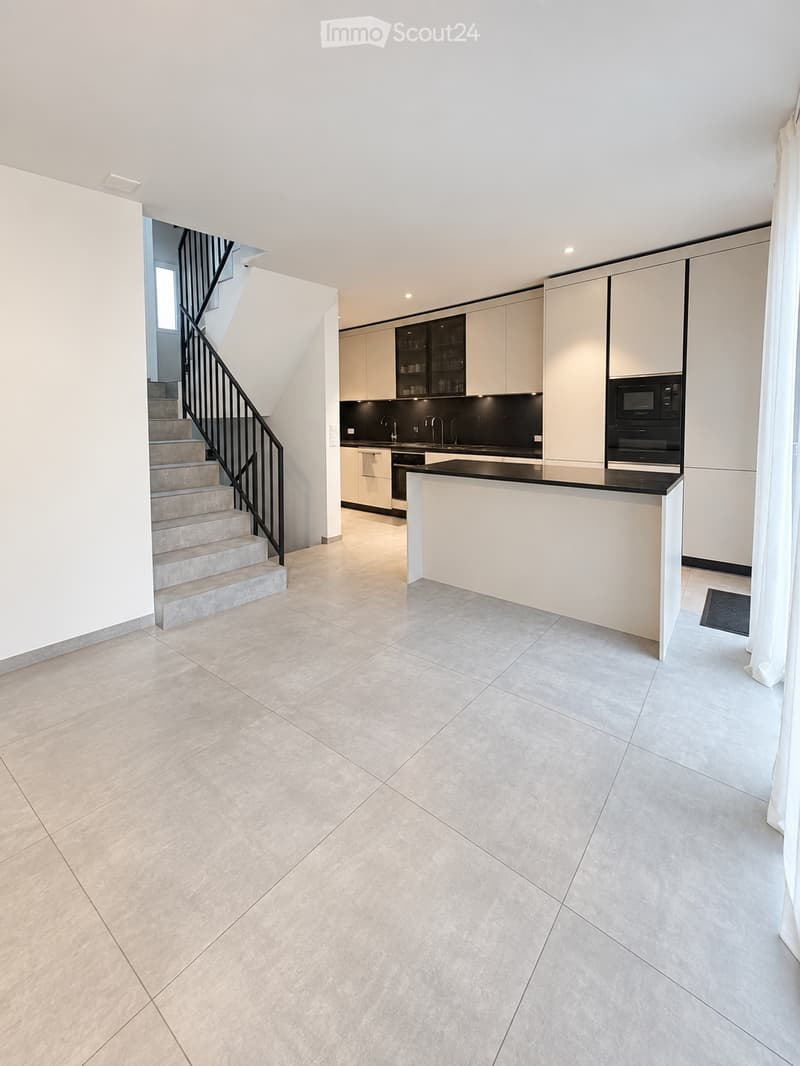 Modern kitchen with white cabinetry, black countertops, a central island, and built-in appliances including a microwave and oven. The space features tiled flooring and a staircase leading upwards.