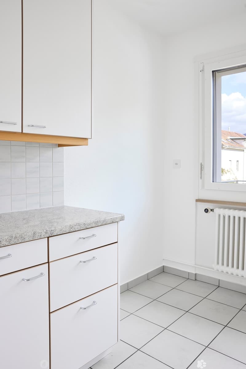Modern kitchen with white cabinets, granite countertop, tiled floor, and a radiator under the window.