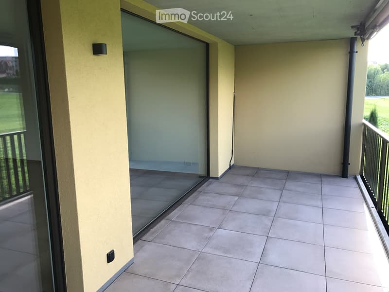 Balcony with tiled floor, glass sliding door, metal railing, and view of greenery.