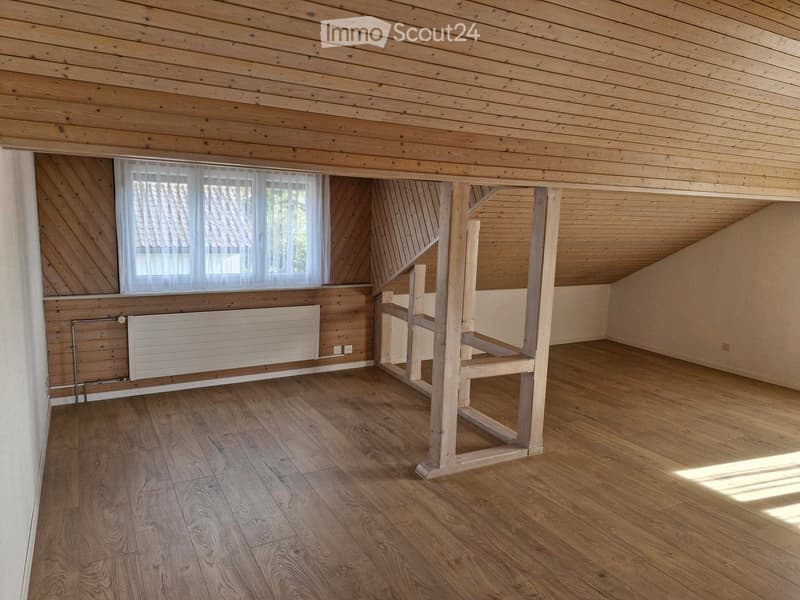 Empty attic room with wooden walls, ceiling, and floor, featuring a window with white blinds and a radiator below it.