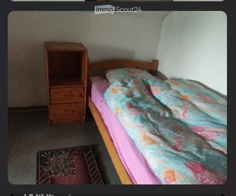 Small bedroom with a single bed, colorful quilt, wooden nightstand, and a small rug on the floor.