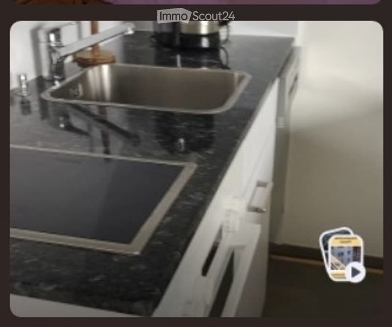Modern kitchen with a black granite countertop, stainless steel sink, and built-in stove. White cabinets and a sleek design.