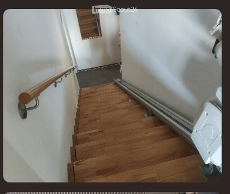 Wooden staircase with handrail and white walls, leading to an upper level.