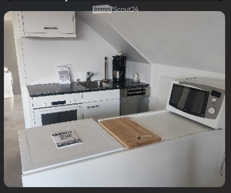 Compact kitchen with white cabinets, grey countertops, sink, oven, microwave, coffee maker, and a wooden cutting board on the counter.
