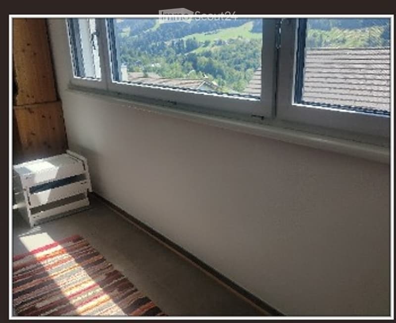 Empty room with large windows offering a scenic mountain view, wooden floor, and a small radiator.