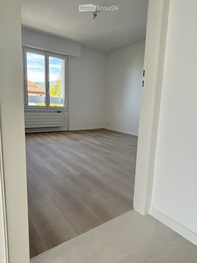 Empty room with wooden flooring, white walls, and large windows offering a view of the outside. No furniture or equipment is present.