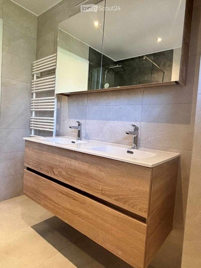 Modern bathroom with a double sink vanity, sleek wooden cabinetry, and a large mirror above. A white radiator is positioned on the left side.
