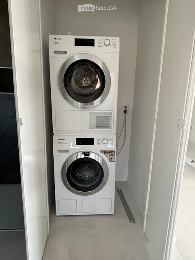Compact room with stacked white washing machine and dryer, clean and organized.