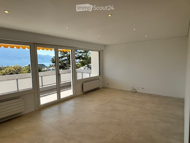 Empty room with large windows offering a scenic view, tiled floor, and white walls.