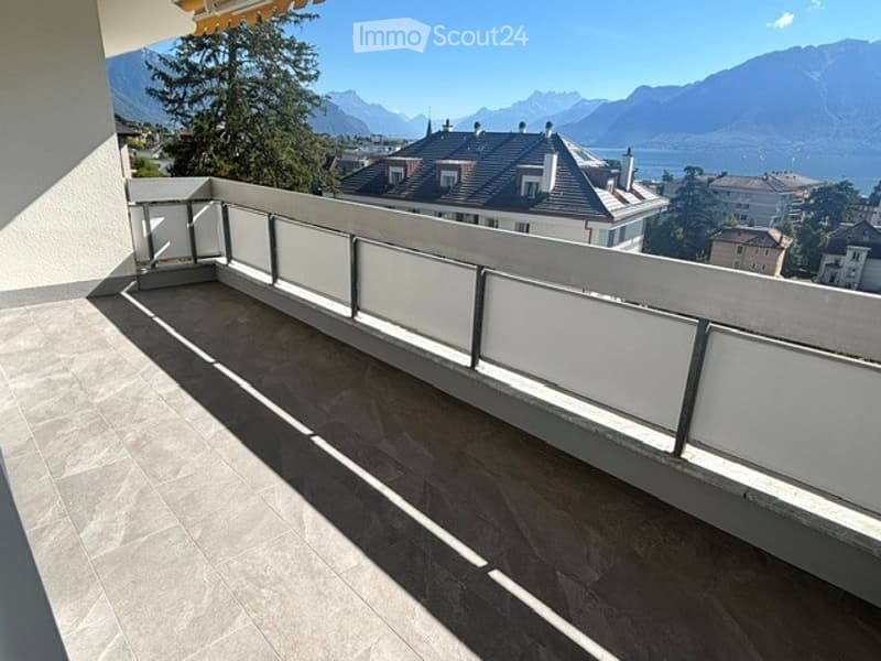 Balcony with a modern white railing, tiled floor, and scenic mountain and lake view in the background.