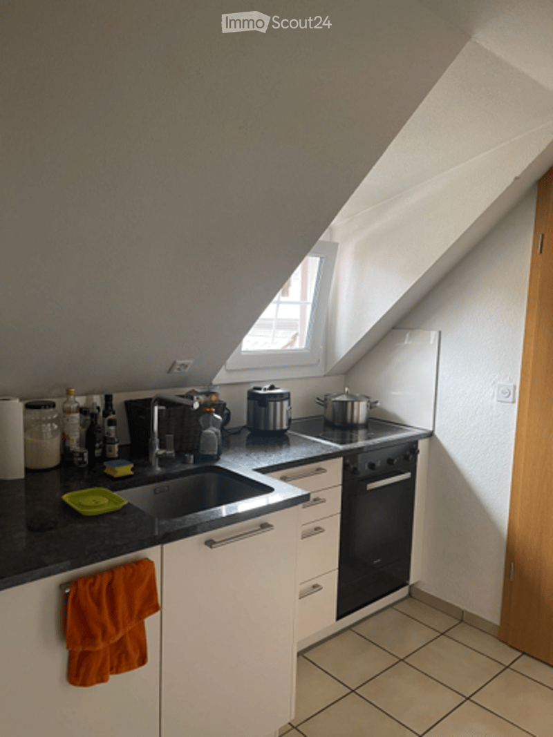 Compact kitchen with white cabinets, black countertop, sink, oven, and various small appliances.