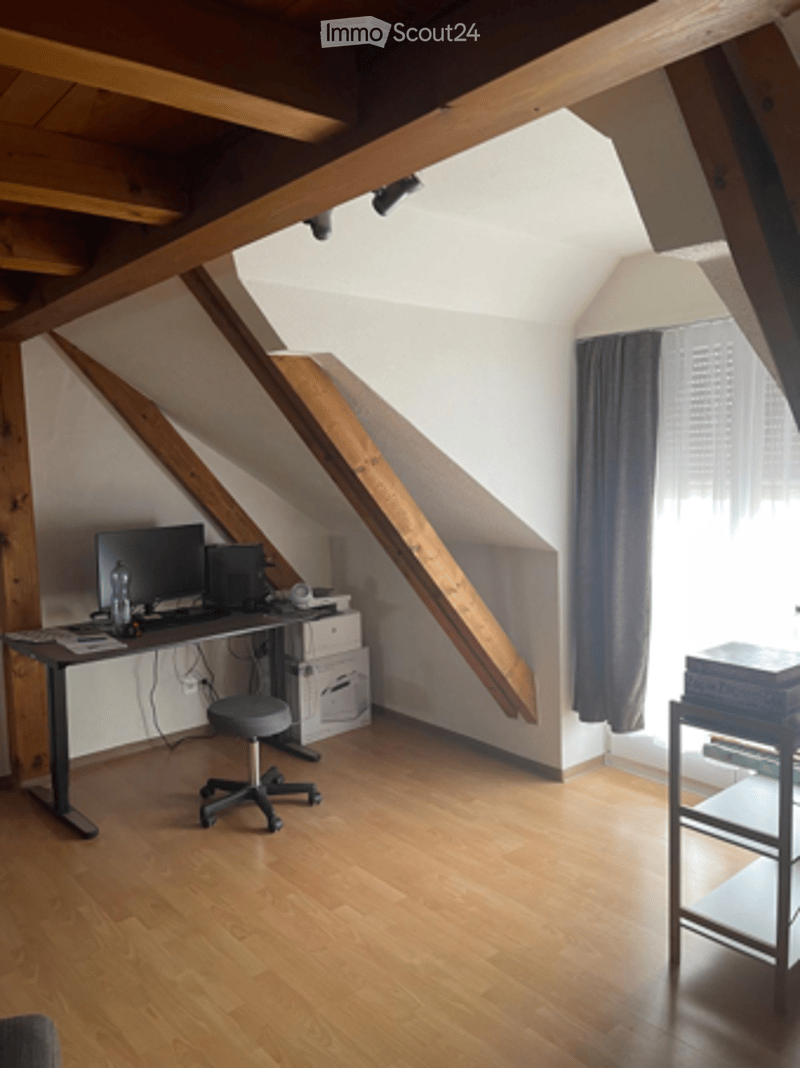 Loft-style room with wooden beams, hardwood floor, desk with computer, chair, and shelf.