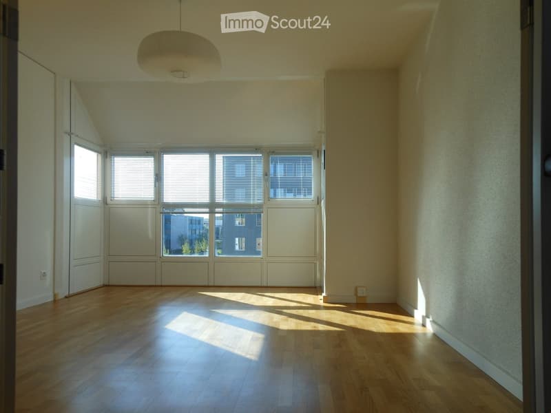Empty room with wooden flooring, large windows with blinds, and a hanging light fixture.
