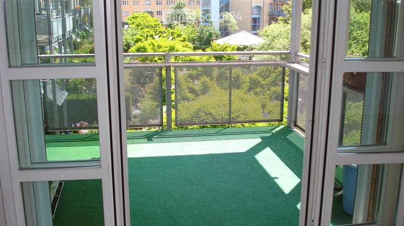 Balcony with green artificial turf flooring, metal safety railing, and open views of surrounding greenery and buildings.