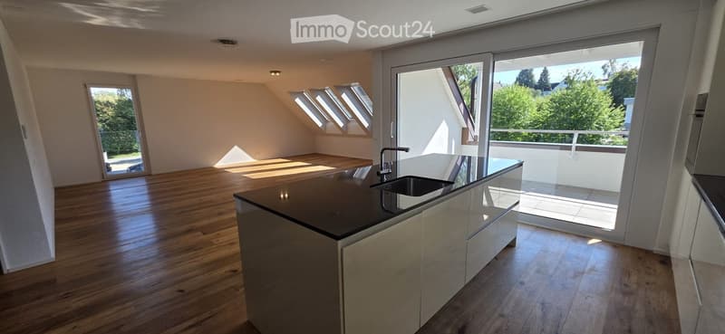 Bright, open kitchen with wooden flooring, modern island, and large windows leading to a balcony.