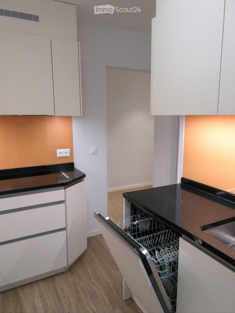 Modern kitchen with white cabinets, black countertop, and an open dishwasher.