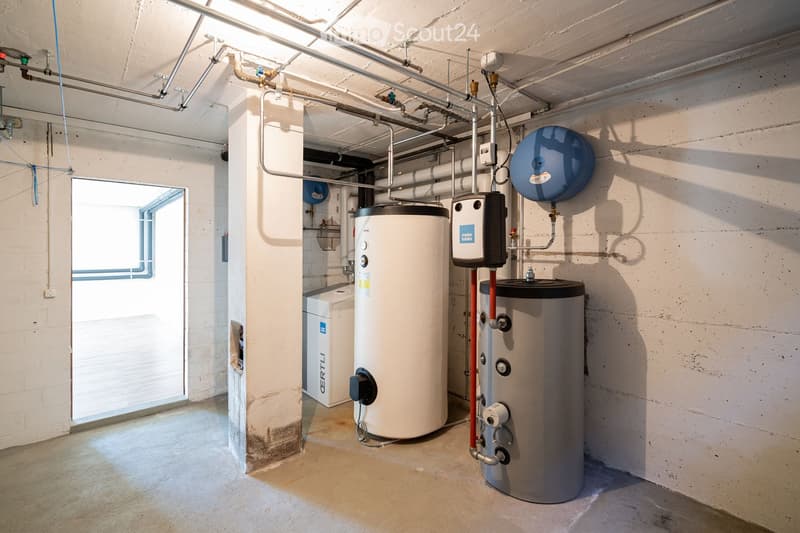 Utility room with water heaters, boilers, control units, and exposed pipes.