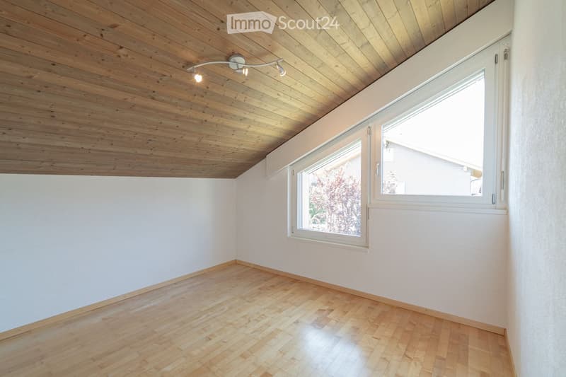 Empty room with wooden flooring, white walls, and a large window with white frame. The ceiling is wooden with built-in lighting.