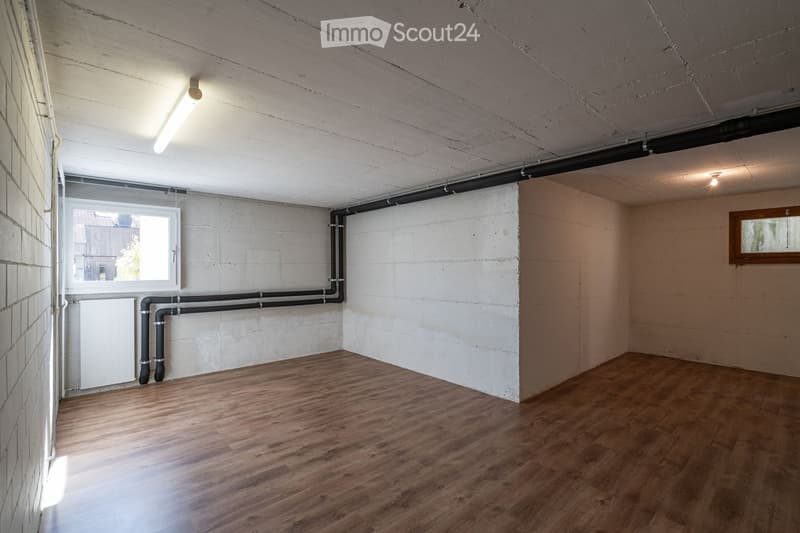 Empty room with wooden flooring, white brick walls, exposed pipes, and two windows providing natural light.