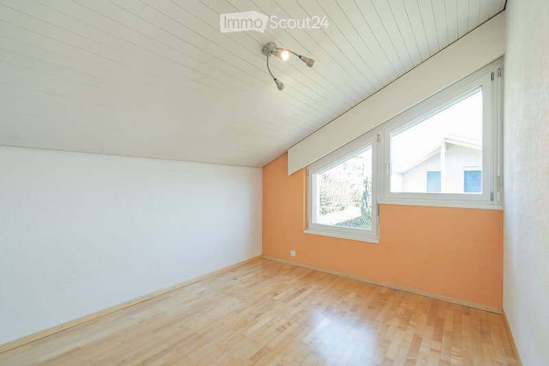 Empty room with wooden flooring, white walls, and a large window with white frame. The ceiling has a modern design with recessed lighting.