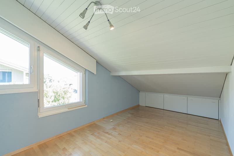 Empty room with wooden flooring, light blue walls, white cabinets, and large windows allowing natural light.
