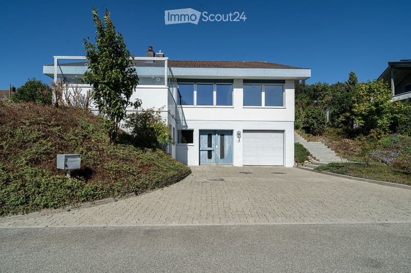 Modern two-story house with white exterior, large windows, garage, and raised ground floor entrance.
