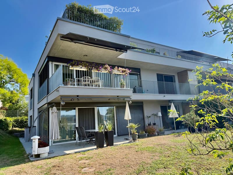 Modern two-story house with balconies, outdoor seating, and greenery.