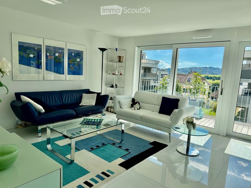 Modern living room with large windows offering a scenic view, two sofas, a glass coffee table, a floor lamp, and decorative shelves.