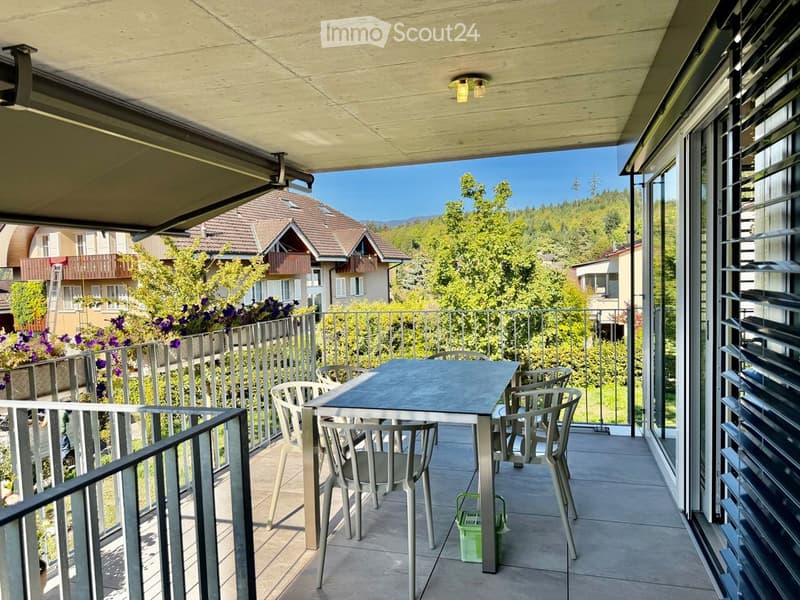 Balcony with a table and chairs, overlooking a scenic view of trees and houses.