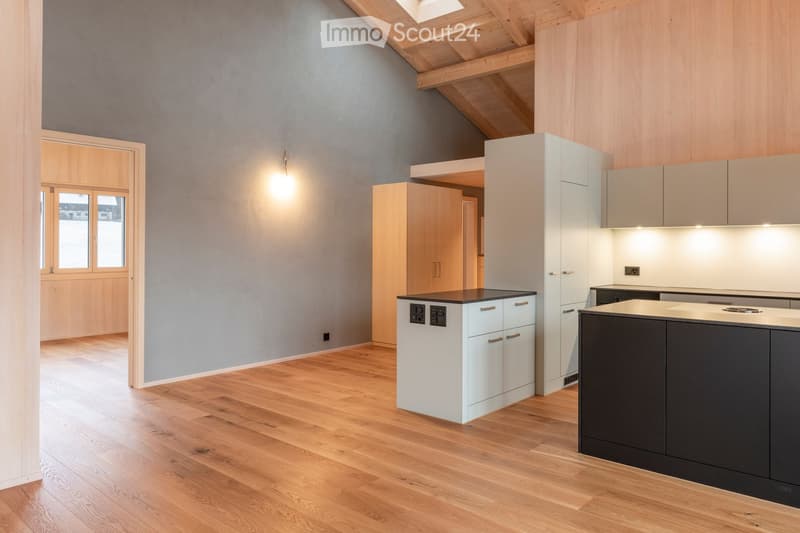 Modern kitchen with light grey walls, wooden flooring, white cabinets, and a dark grey island.