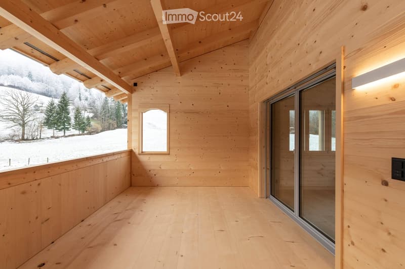 Bright, minimalist room with light wooden walls, ceiling, and floor, featuring large glass windows and a sliding door leading to a snowy outdoor view.