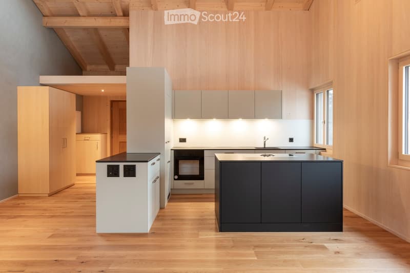 Modern kitchen with light wood walls, white cabinets, dark countertops, and a central island. Features an oven, sink, and faucet.