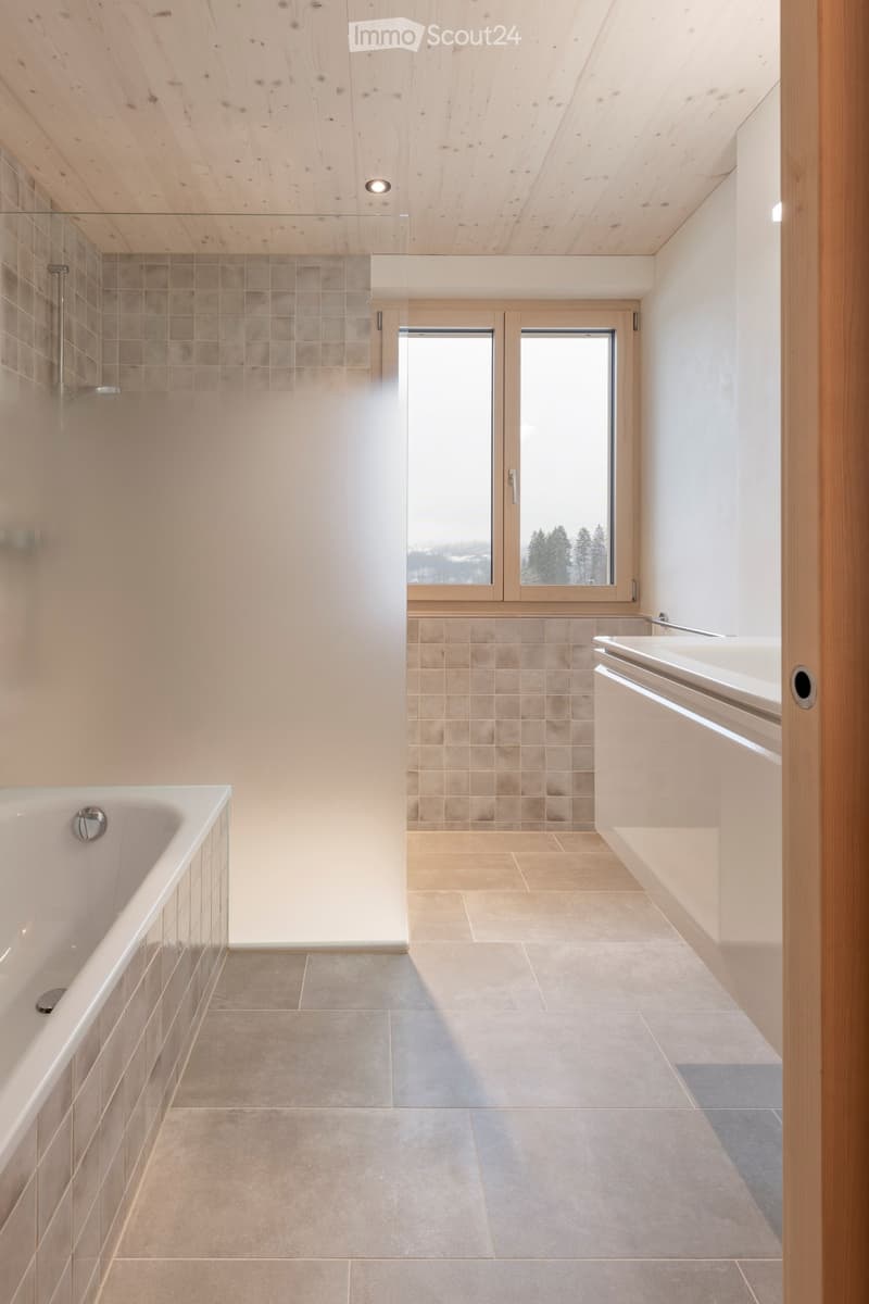 Modern bathroom with a bathtub, sink, and large windows offering a scenic view.