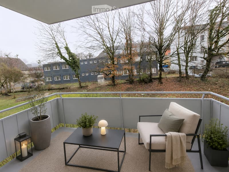 Modern balcony with a white lounge chair, small black coffee table, potted plants, a floor lamp, and a candle lantern.
