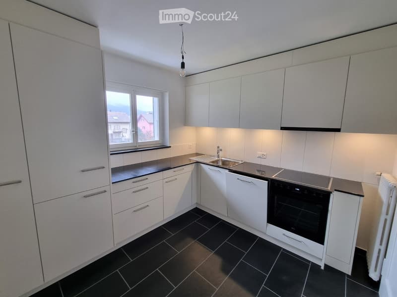 Modern kitchen with white cabinets, black countertops, and black tiled floor. Features a sink, oven, and built-in lighting.