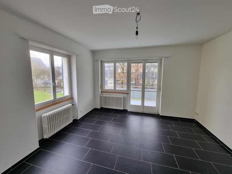 Empty room with dark tiled floor, white walls, large windows, radiators, and a hanging light fixture.