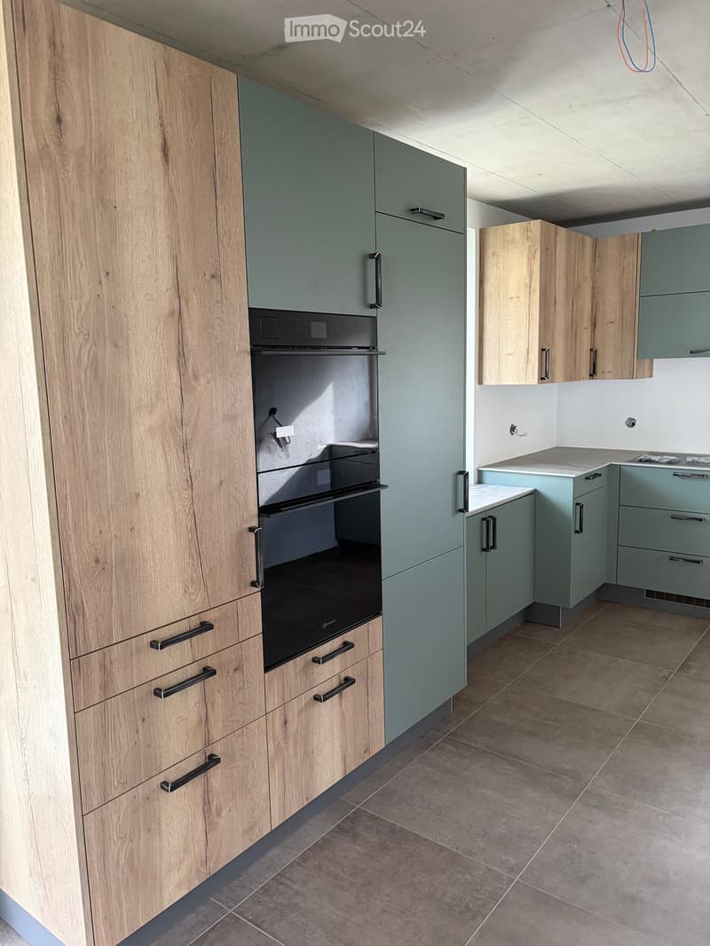 Modern kitchen with light wood and grey cabinets, stainless steel oven, and tiled floor.