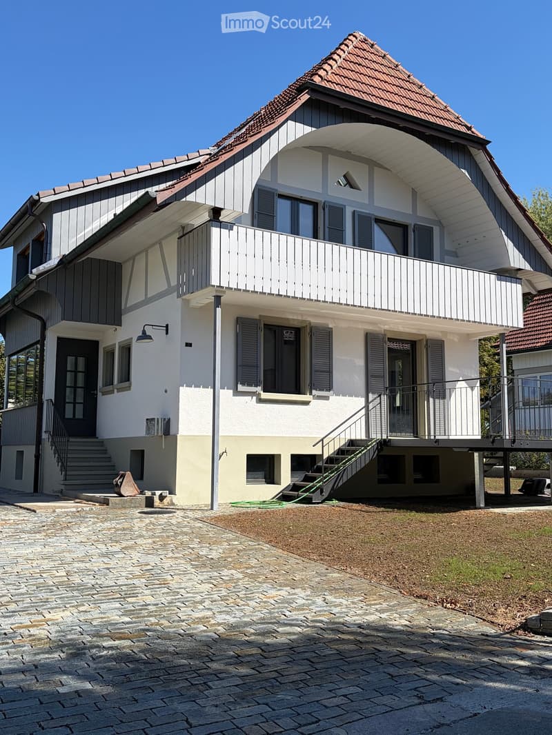 Two-story house with a red-tiled roof, white and grey exterior, large balcony, and modern design.