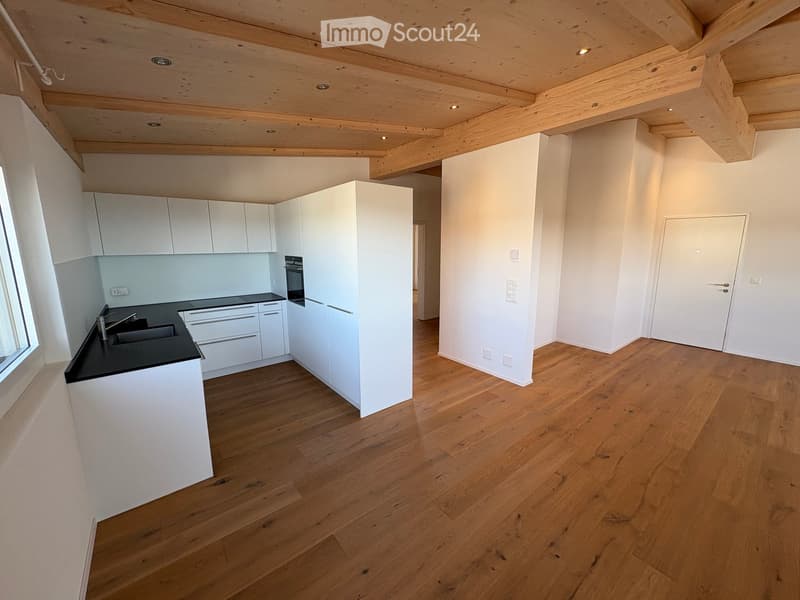 Modern kitchen with white cabinets, black countertop, wooden flooring, and exposed wooden ceiling beams.